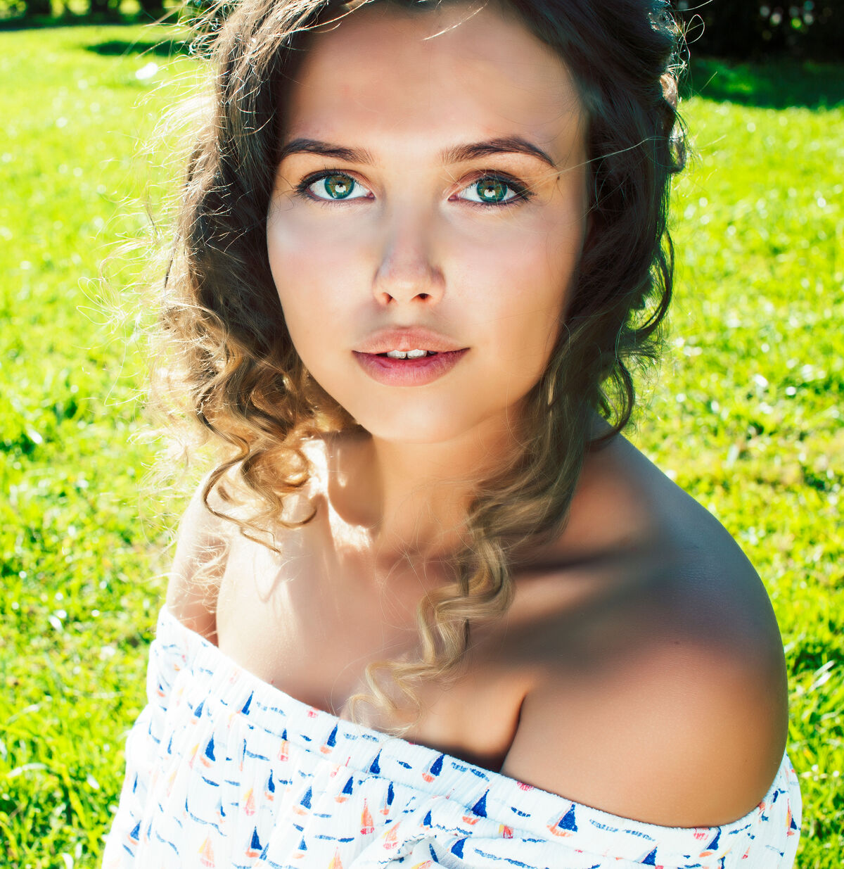 A woman sitting in green grass on a sunny day, peaceful expression.