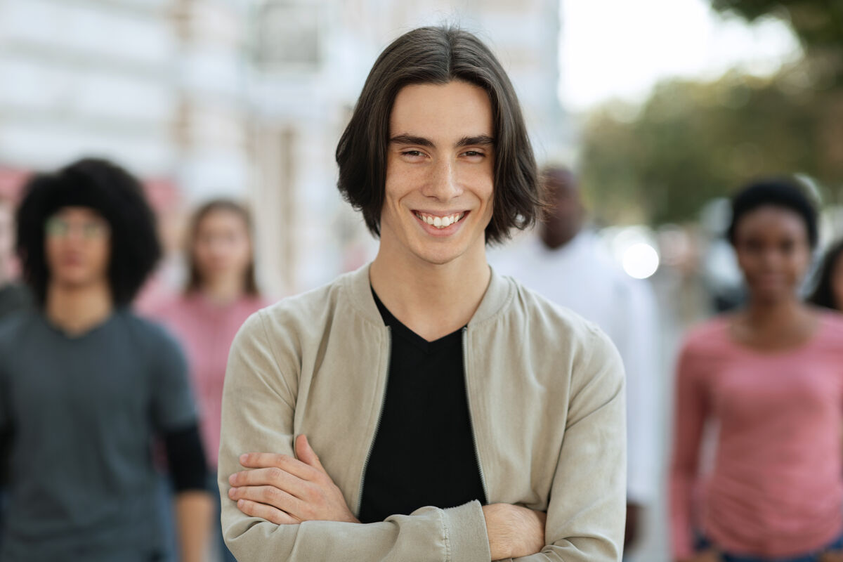 A young man standing thoughtfully in front of a blurred crowd of people on a sunny city street.